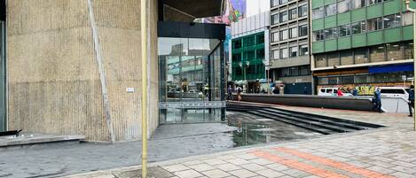 Une rue moderne en milieu urbain, avec un immeuble doté de grandes fenêtres en verre et d’une structure métallique au-dessus.