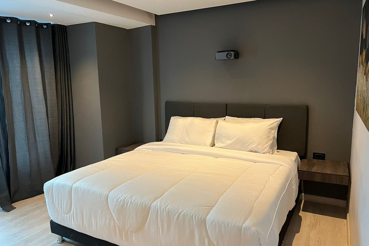 Un dormitorio moderno con una cama grande, paredes oscuras y un proyector instalado en el techo.