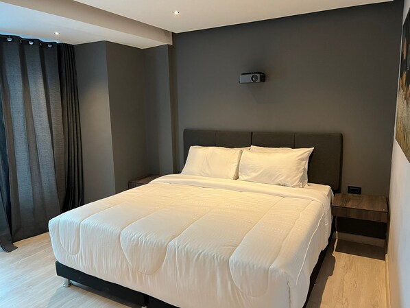 Un dormitorio moderno con una cama grande, paredes oscuras y un proyector instalado en el techo.