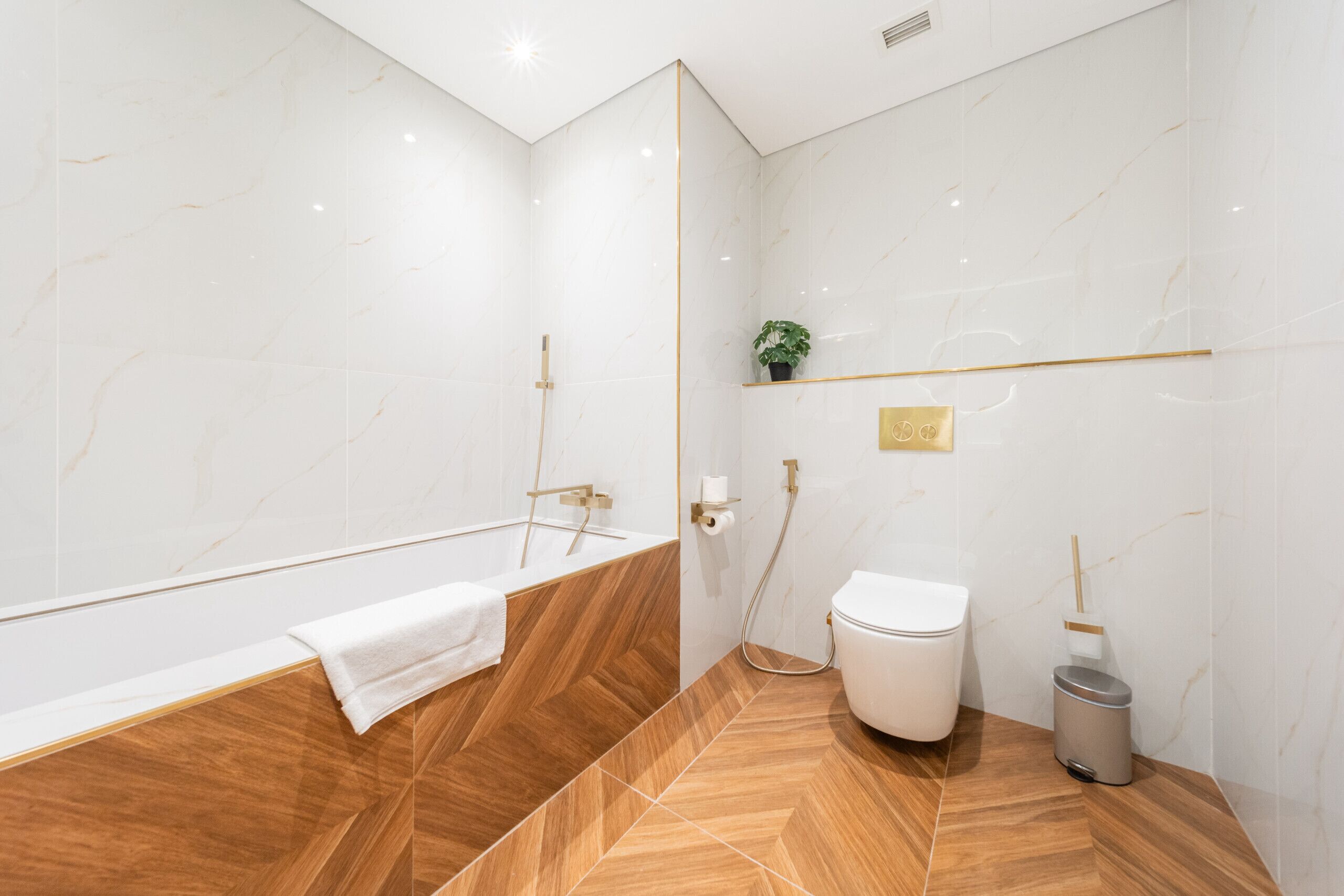 A modern bathroom with a wooden bathtub, white toilet, and a small trash bin.