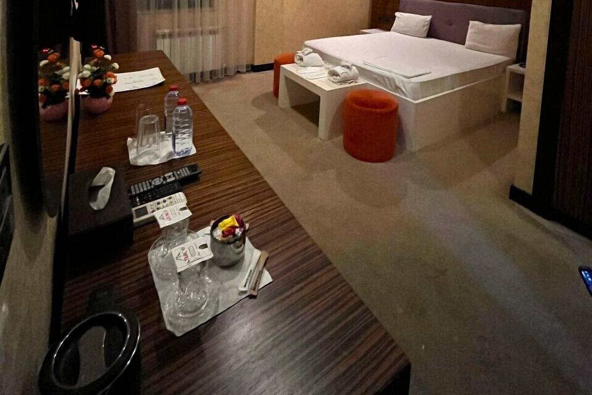 Habitación de hotel con una cama, un escritorio con computadora, un espejo, una ventana con cortinas y un cuadro en la pared.