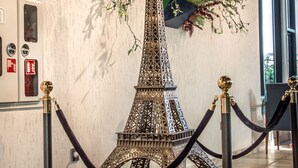 Un modelo de la Torre Eiffel con una barrera de cuerda al frente, sobre un muro texturizado que muestra señales de alarma de incendios y salidas de emergencia.