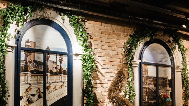 Un restaurante con mesas dispuestas para comer, amplias ventanas arqueadas y vistas a un puente.