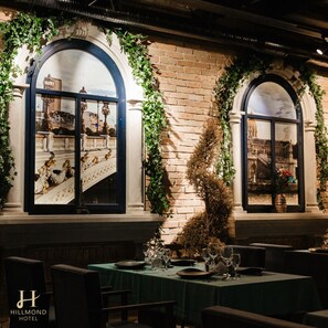 Un restaurant avec des tables dressées pour le service, de grandes fenêtres en arc de cercle et une vue sur un pont.