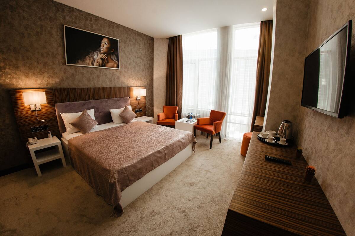 Habitación de hotel con una cama grande, mesitas de noche, un escritorio con silla, televisor y ventana con cortinas.