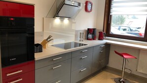 Uma cozinha moderna com geladeira Bosch, forno embutido, pia de aço inoxidável e um banquinho vermelho.