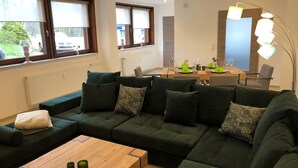 Uma sala de estar moderna com um sofá seccional, uma mesa de centro de madeira e uma área de jantar com mesa posta para quatro pessoas.