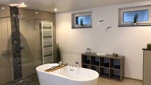 Um banheiro moderno com uma banheira de pedestal, chuveiro com box de vidro e toucador com prateleiras abertas.