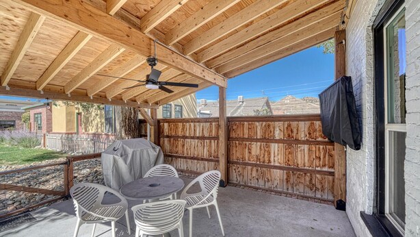 A covered patio with a ceiling fan, a table with chairs, and a barbecue grill.
