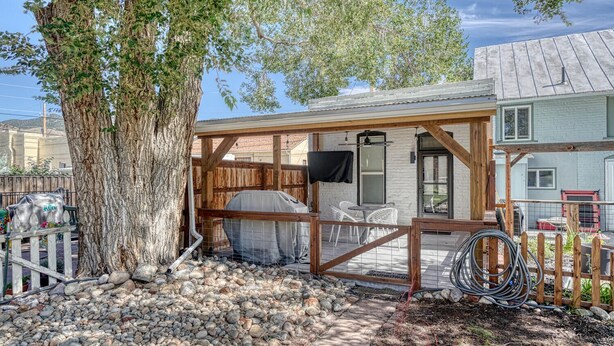 A rustic outdoor patio with a wooden pergola, a barbecue grill, and a seating area with white chairs. - The Brick Unit B on F st Downtown Salida! (Salida)