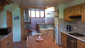 Une cuisine avec des meubles de rangement en bois, une table à manger et un four encastré.
