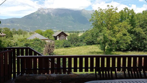 Une terrasse en bois avec un mur en pierre, offrant une vue sur un paysage montagneux sous un ciel dégagé.