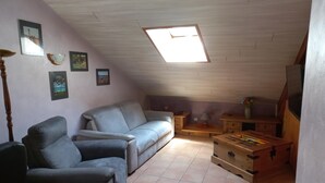 Une pièce mansardée chaleureuse, avec un plafond en pente, un canapé, un fauteuil, une malle en bois et une petite table.