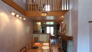 Un espace repas avec une table et des chaises en bois, un escalier et une cuisine en arrière-plan.