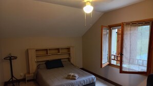 Une chambre à coucher avec un lit, une tête de lit en bois, un bureau, une chaise et une fenêtre avec des rideaux.