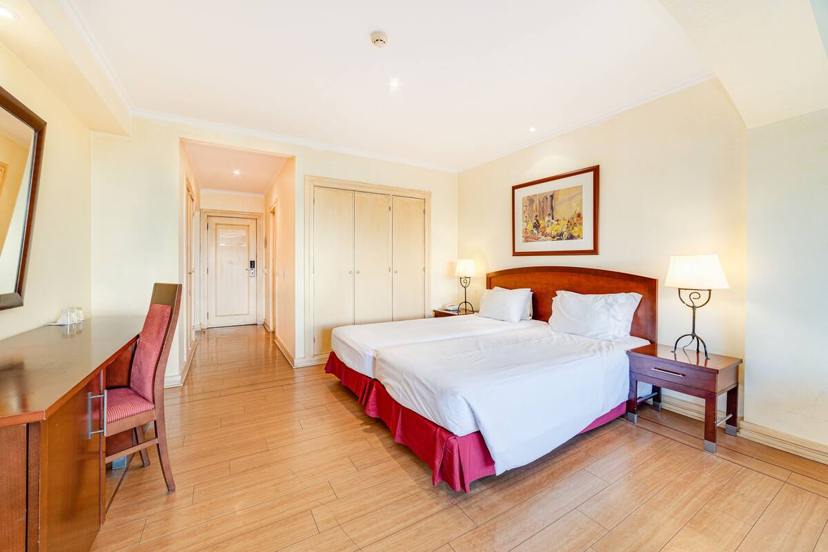 Habitación de hotel con una cama grande, un escritorio, una silla y una mesita de noche con lámparas.