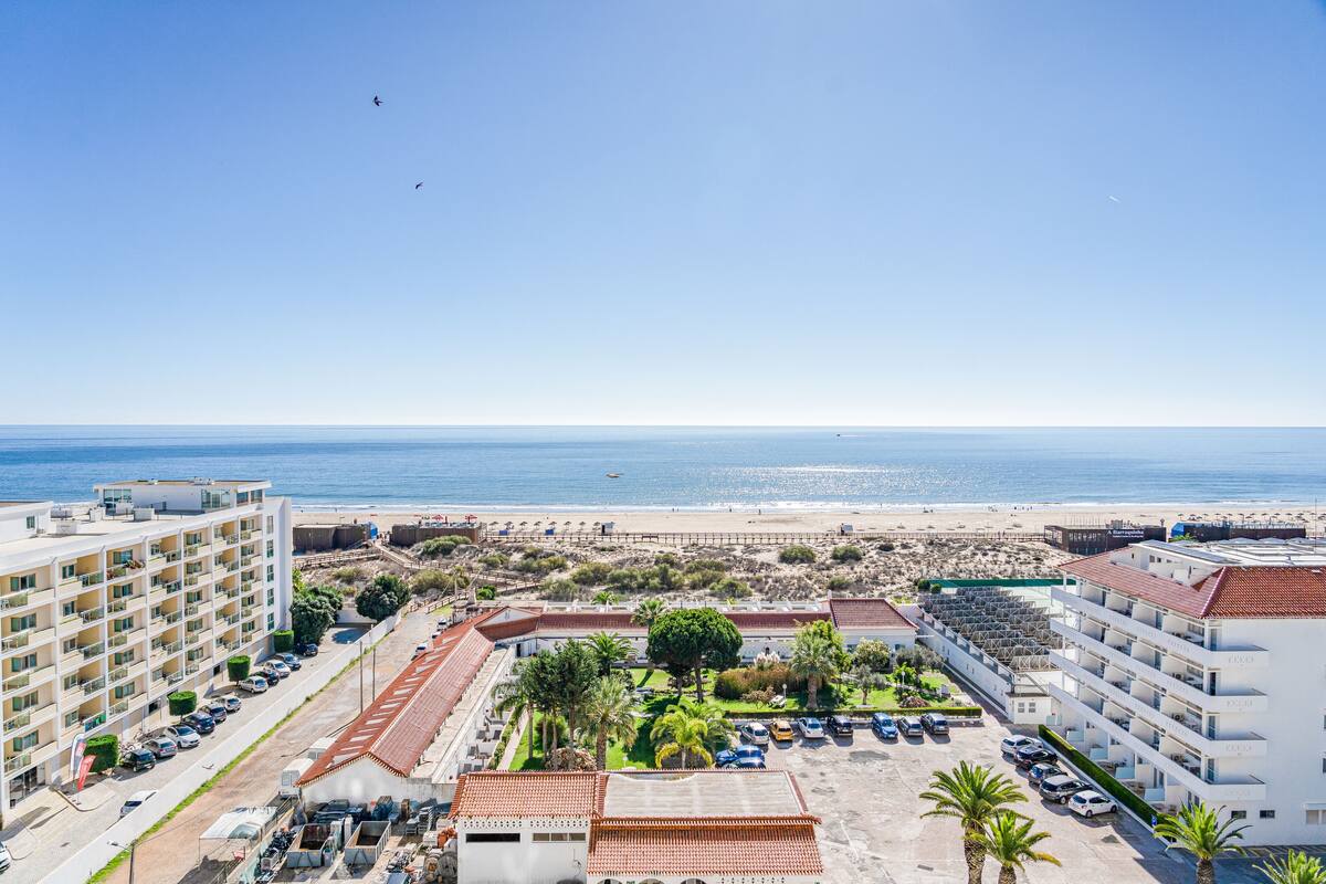 Un hotel costero con varios pisos, zona de estacionamiento y vista a la playa.