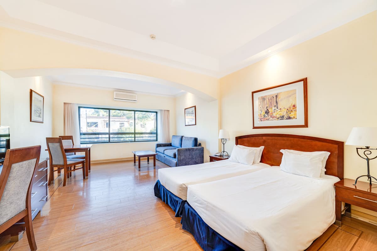 Habitación de hotel con dos camas, un sofá, un escritorio con sillas y un ventanal con vistas.