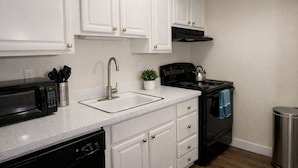 A kitchen with white cabinets, a stainless steel sink, a black stove, and a microwave.