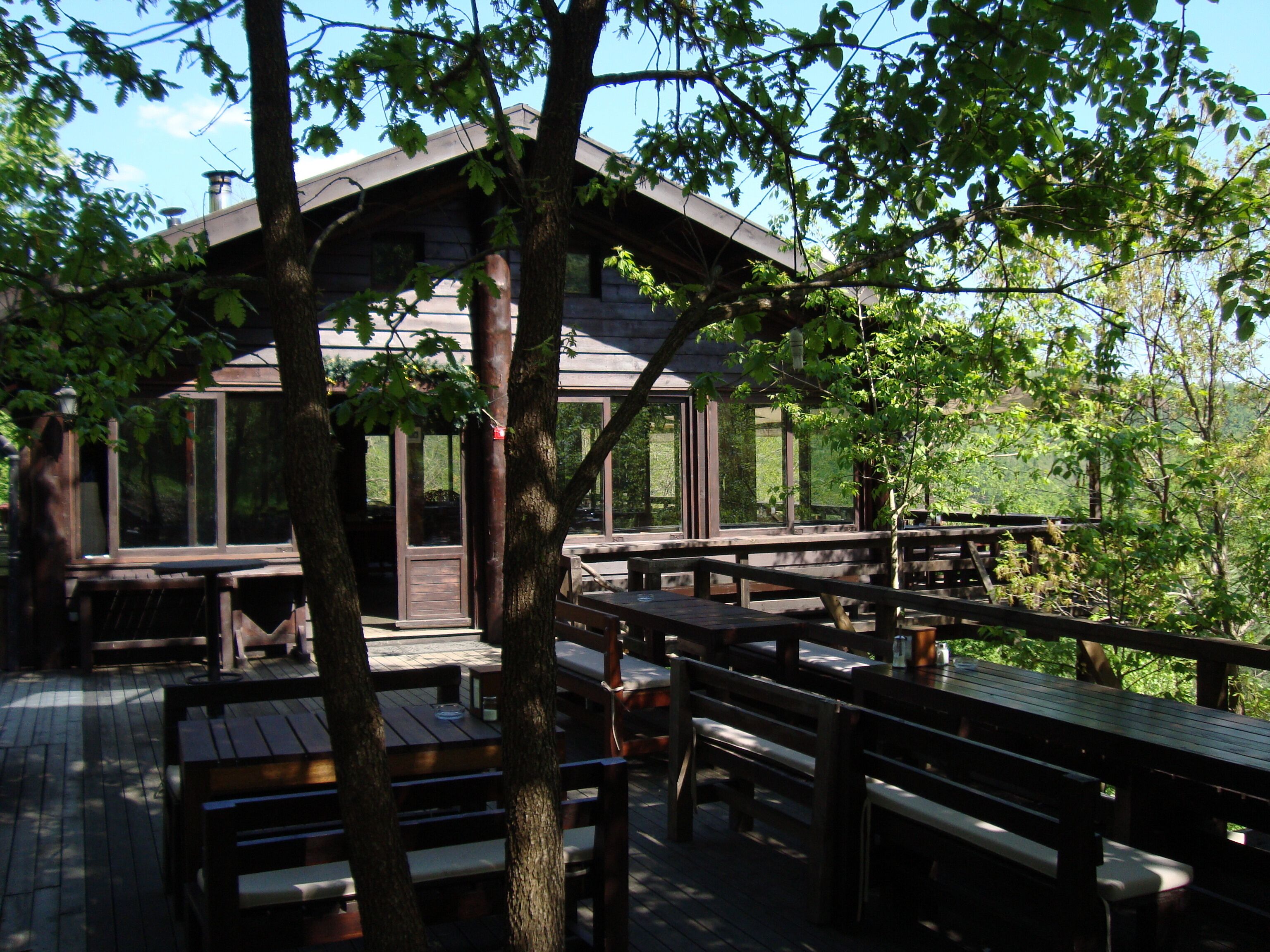 An outdoor wooden deck with picnic tables and benches, surrounded by trees.