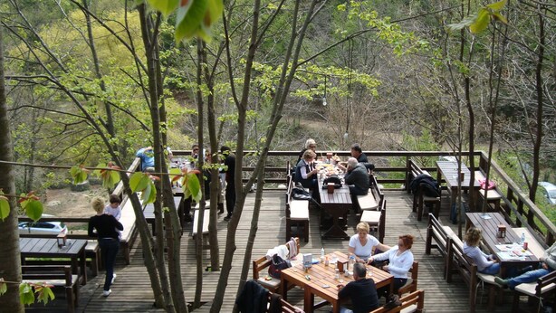 An outdoor wooden deck with picnic tables and benches, surrounded by trees. - Kulindağ Dağ Evi (Beykoz)