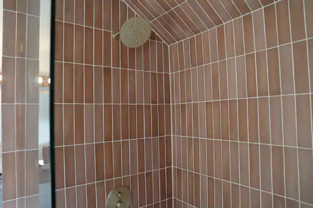 Une zone de douche carrelée, équipée d’un pommeau de douche et d’un robinet de réglage.