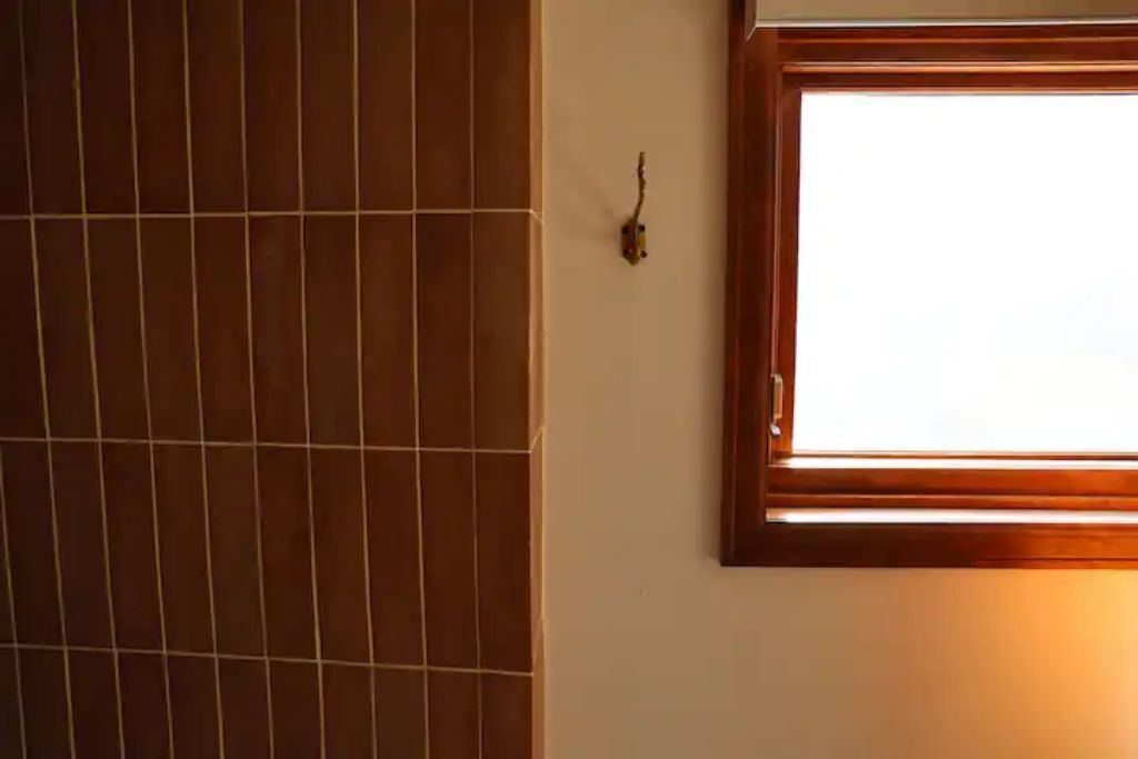 A bathroom with a tiled wall and a window with a wooden frame.