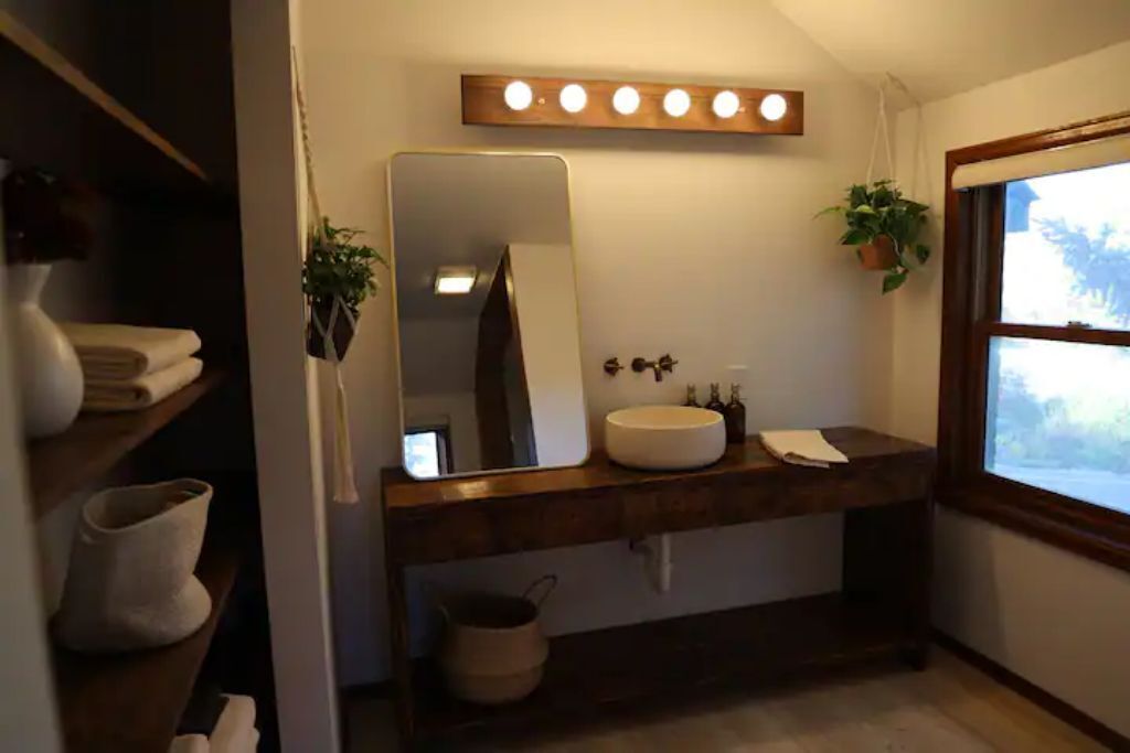 A bathroom with a wooden vanity, a large mirror, a sink, and a window. There are towels and a potted plant on the vanity.