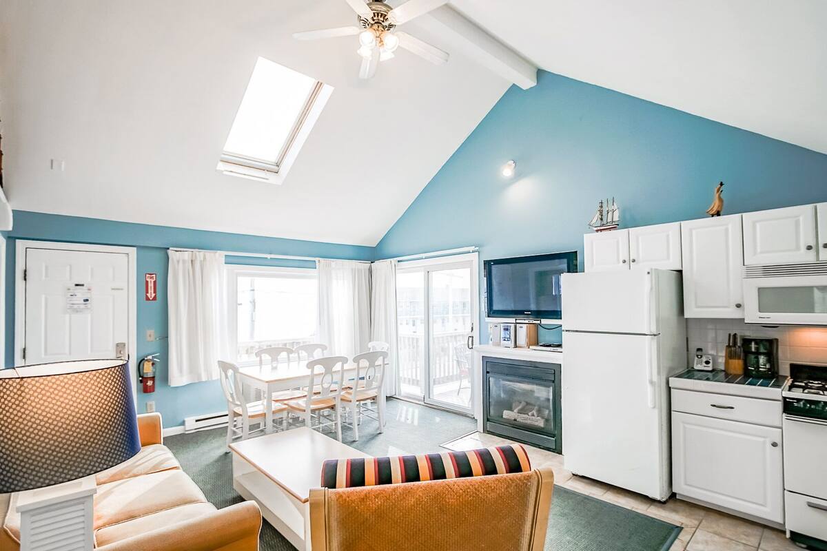 A compact living space with a dining area, kitchenette, and a large window providing natural light.