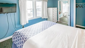 A bedroom with a bed, a dresser, a television mounted on the wall, and a window with curtains. - Seawinds II (Dennis Port)