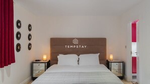 Een slaapkamer met een bed, twee nachtkastjes met lampen, een hoofdbord met een logo en een rood gordijn.