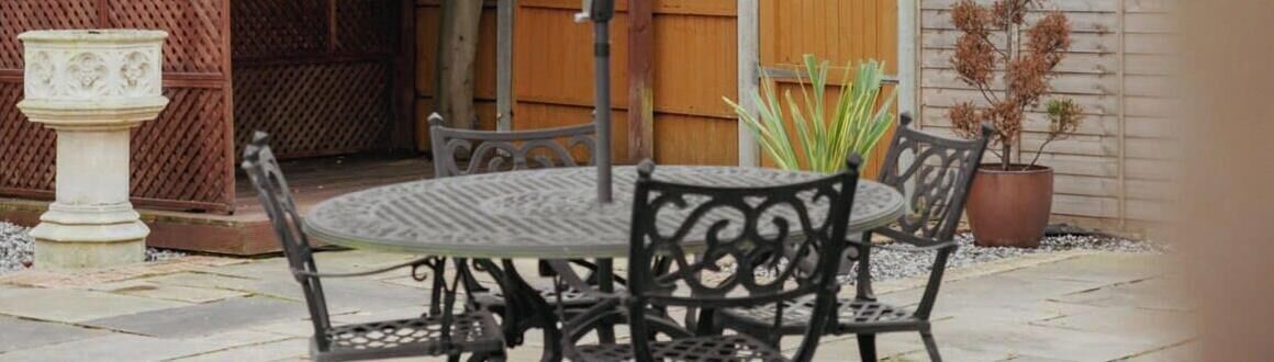 An outdoor patio with a round table and four chairs, surrounded by potted plants and a decorative urn.