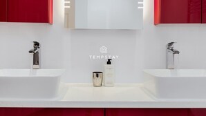 Een moderne badkamer met twee wastafels, een spiegel en rode kastjes.