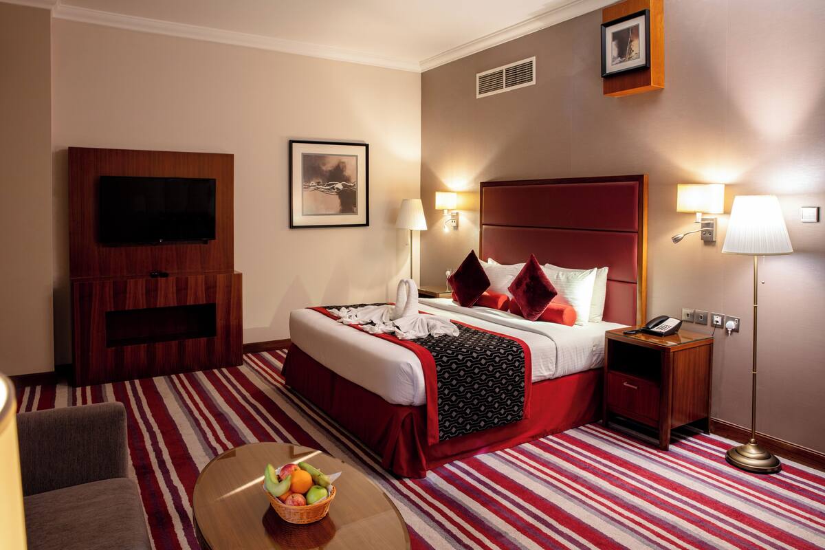 Une chambre d’hôtel avec un grand lit, un téléviseur à écran plat, un bureau avec une lampe et un panier de fruits.