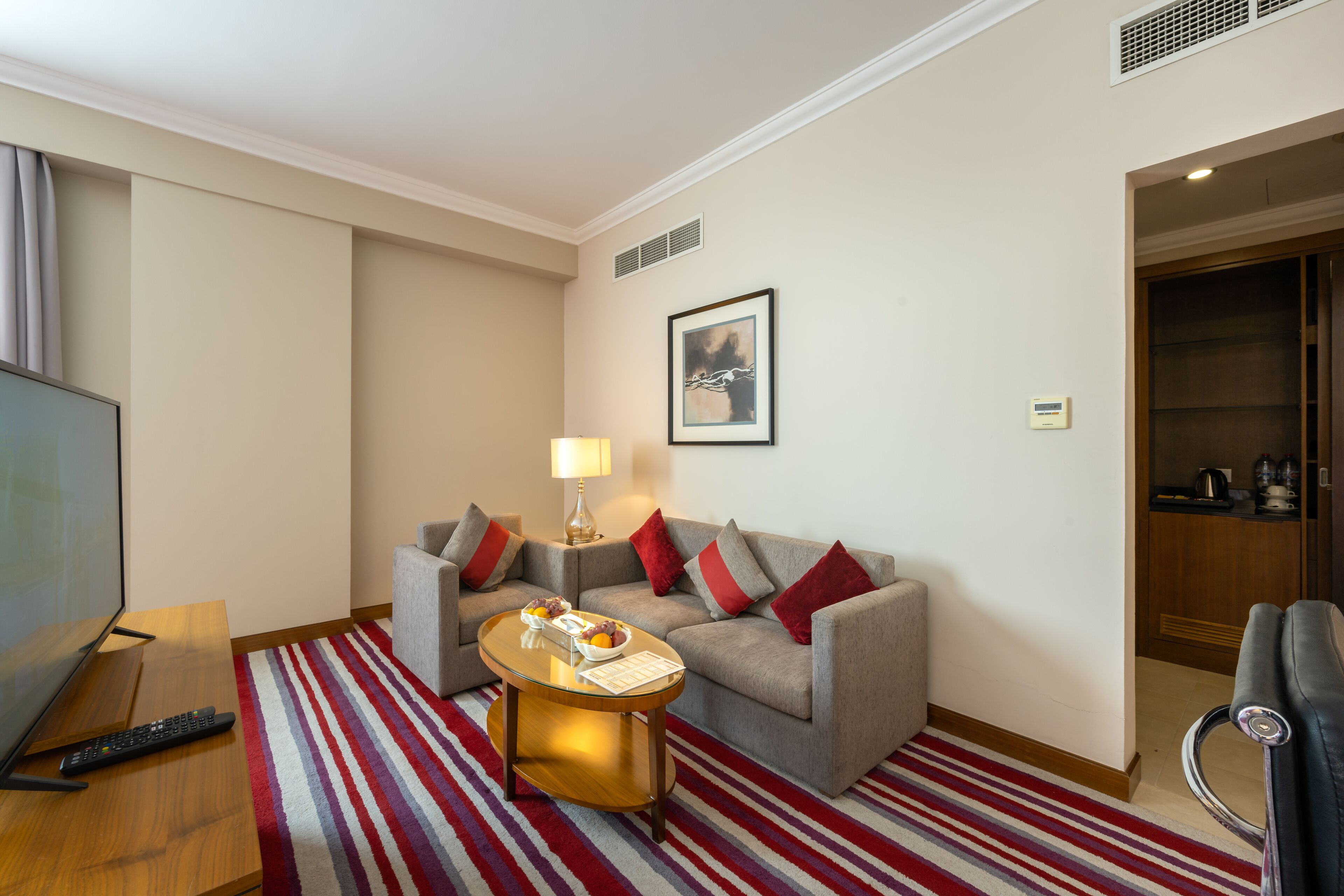 A hotel room with a sofa, a coffee table, a TV, and a red-striped rug.