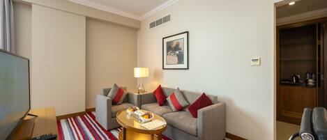 A hotel room with a sofa, a coffee table, a TV, and a red-striped rug.