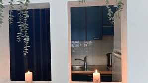A window with a candle and hanging greenery, a kitchen visible through the window with dark cabinets and a sink. - IzzHome City Love (Cagliari)