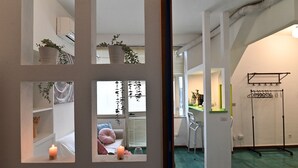 A hallway with a mirrored wall, potted plants, a bed with pillows, and a hanging rack. - IzzHome City Love (Cagliari)