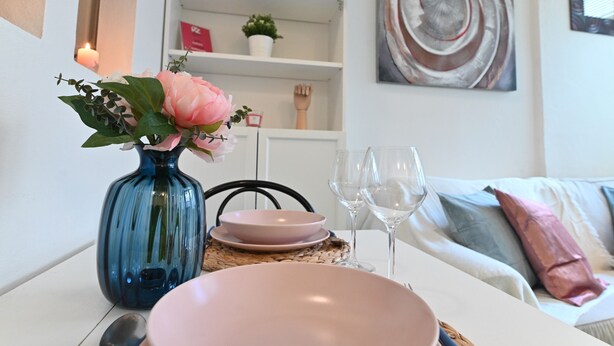 A dining table with a vase of flowers, pink plates, and wine glasses. - IzzHome City Love (Cagliari)