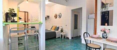 A modern living room with a bed, a dining table with chairs, and a kitchenette area.
