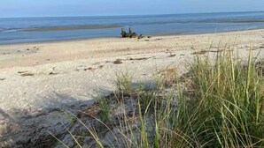 A beach with sand, grass, and a clear sky.