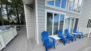 A covered deck with blue Adirondack chairs and a small table, adjacent to a building with large windows and a white railing.
