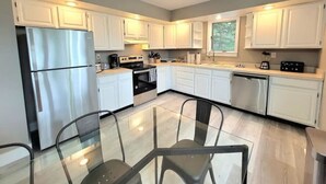 A modern kitchen with white cabinets, stainless steel appliances, and a glass dining table.