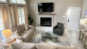 A living room with a sofa, armchair, coffee table, fireplace, TV, and a door. - Chalet By The Bay - Sleeps 12 (Lower Township)