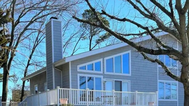 A two-story house with a balcony, a chimney, and a deck. - Chalet By The Bay - Sleeps 12 (Lower Township)