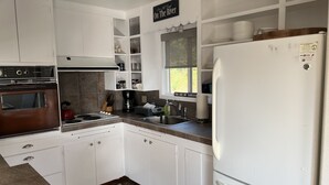 Una cocina con gabinetes blancos, un lavamanos de acero inoxidable, una cafetera negra y un refrigerador blanco.