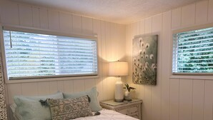 Un dormitorio con cama, almohadas, una mesita de noche, una lámpara y un cuadro.