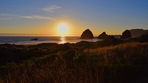 Un paisaje costero con un atardecer, que presenta formaciones rocosas destacadas y un primer plano con césped.