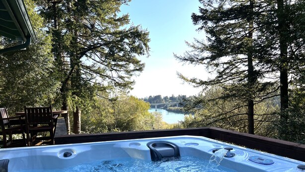 Un jacuzzi con vista a un río y un puente, rodeado de árboles.