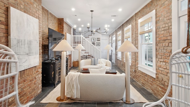 A narrow hallway with exposed brick walls, white railings, and a staircase leading to an upper level.